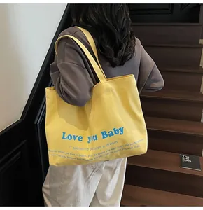 Detail of yellow canvas tote bag with blue 'Love you Baby' lettering and dual shoulder straps
