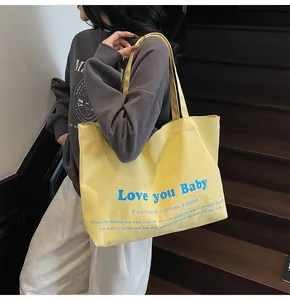 Close-up of yellow canvas tote bag featuring 'Love you Baby' blue lettering text on a model