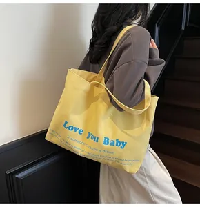 Detail of yellow canvas tote bag with Love You Baby blue text print and long shoulder strap