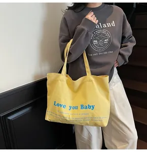 Detail of a bright yellow canvas tote bag with blue 'Love you Baby' art text print