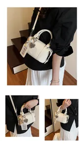 Close-up of off-white lychee leather boston bag with embossed letters and heart charm