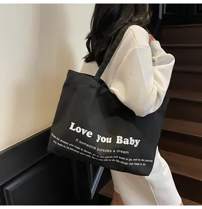 Lifestyle shot of large black canvas tote bag with white lettering on casual white outfit