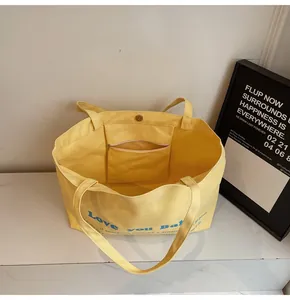 Detail view of large yellow canvas tote bag showing magnetic snap and zip pocket
