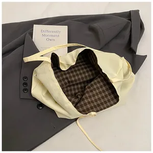 Detail of canvas tote bag showing cream exterior and brown plaid lining on a blazer