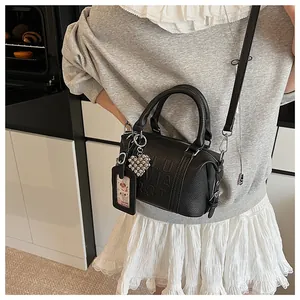 Detail of black pebbled leather cylinder bag with embossed letters and heart charm