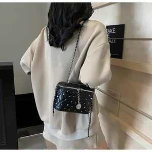 Detail of black quilted mini box bag with pearl studs and silver chain strap worn by model