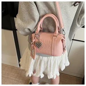 Pink lychee grain Boston bag with heart charm and card holder worn by a model
