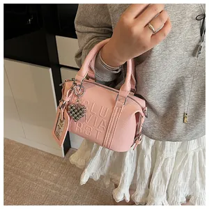 Detailed close-up of pink litchi grain leather bag with embossed letters and heart charm