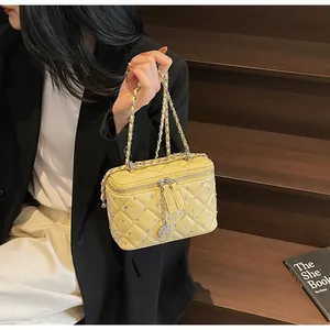 Detailed view of yellow quilted box bag featuring silver studs and floral charm pendant