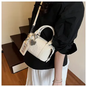 Detail of cream Boston bag featuring pebble leather, embossed letters, and a heart charm