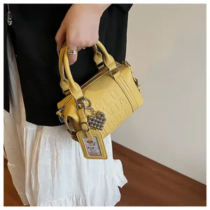 Detail of ginger yellow boston bag with embossed letters and heart-shaped pendant charm