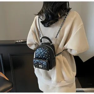 Close-up of black quilted mini backpack with silver rivets and metal chain straps