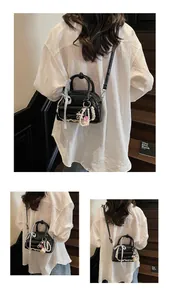 Détail du sac à main noir brillant avec nœud, chaîne de perles et bord en dentelle