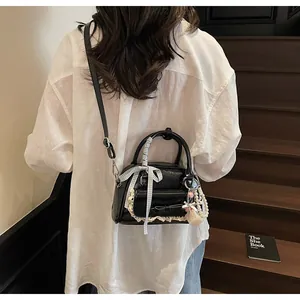 Détail d'un sac bandoulière en cuir verni noir avec nœud à carreaux gris et dentelle