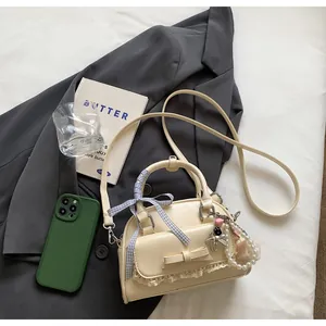 Détail du sac crème avec nœud, dentelle, breloque perle et ruban à carreaux bleus