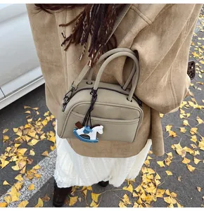 Close-up of a stylish khaki boston bag with a trojan charm on autumn gingko leaves background