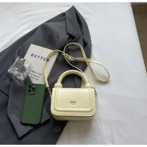 Detailopname van de crème lederen mini handtas met goud logo op grijze blazer
