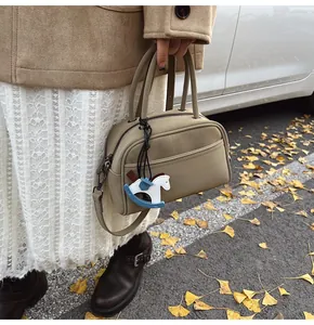 Close-up of khaki Boston bag with horse charm, silver hardware, and detachable strap