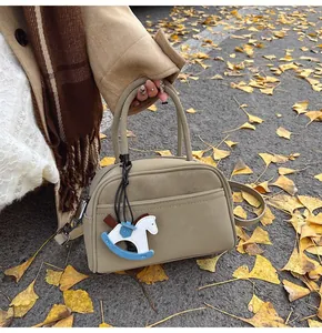 Detail of beige crossbody pillow bag with horse charm on autumn leaves background