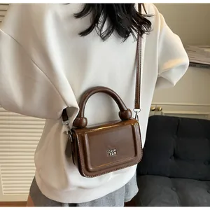 Detail van glanzende bruine crossbodytas met unieke ronde handgreep gedragen door model