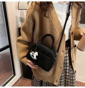 Close-up of black crossbody bag with horse pendant on a fashionably dressed model