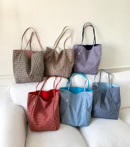 Detailed view of six colorful double-sided checkered nylon tote bags on white sofa