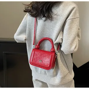 Detail van de rode lederen crossbodytas met glanzende afwerking en zilveren metalen logo