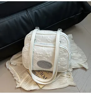 Gros plan sur la texture florale embossée blanche et le logo argenté du petit sac carré