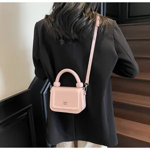 Model met een kleine lichtroze handtas met ronde handgreep en afneembare schouderriem