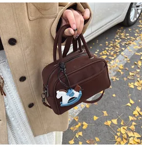 Detail of a dark brown leather pillow bag with a horse charm in an autumn outdoor setting
