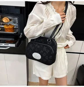 Détail du sac bandoulière jacquard floral noir avec double fermeture éclair et plaque logo