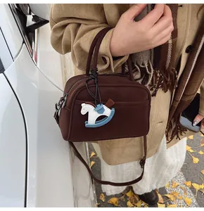 Close-up of a vintage brown leather pillow bag with a horse charm and adjustable strap