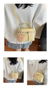 Close-up of cream yellow textured handbag with silver zipper and cute teddy bear pendant
