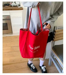Detail of red canvas tote bag featuring white artistic lettering and red checkered lining