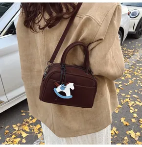 Detail of a dark brown crossbody pillow bag with horse charm in a street style setting
