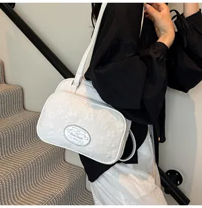 Détail de la texture florale en relief et du logo en cuir sur le sac à bandoulière blanc