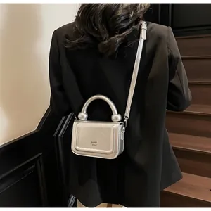 Detailopname van een zilveren vierkante mini-tas met rond handvat op zwarte blazer