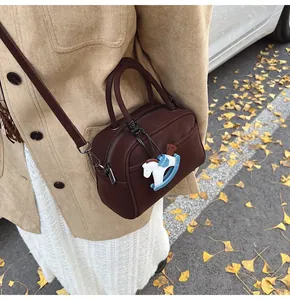 Detail of a dark brown mini pillow bag with a rocking horse pendant and adjustable strap