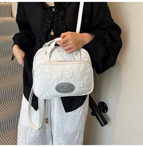 Détail de la broderie florale blanche et du logo en métal argenté sur un petit sac carré