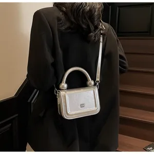 Detail van zilveren metallic mini-tas met cilindrisch handvat en afneembare riem