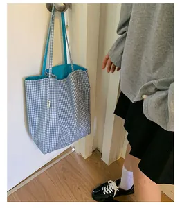 Detail of blue and white gingham tote bag with brand label hanging on a door handle