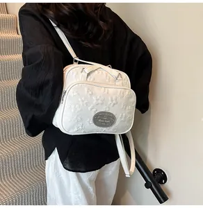 Détail d'un sac à bandoulière blanc avec broderies florales 3D et plaque logo argentée