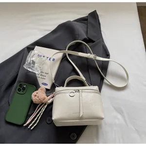 Close-up of off-white leather bag with cracked texture, silver ring zip and bear charm