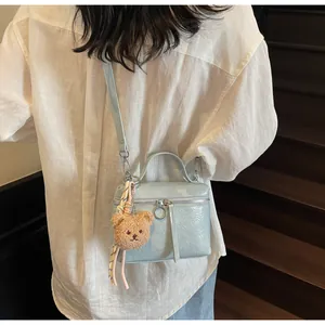Detail view of light blue cracked leather bag with plush bear charm on wooden stairs