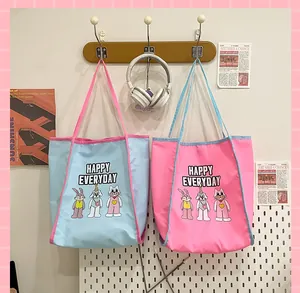 Détail de sacs cabas bicolores en toile avec motif lapin sur crochets en bois