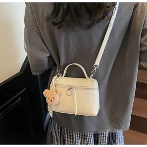 Detail of cream mini handbag featuring glossy textured leather and a cute bear charm