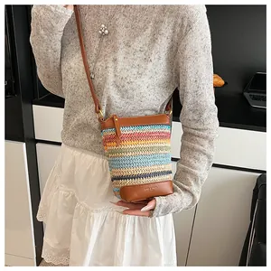 Close-up of rainbow striped woven crossbody bag with brown faux leather trim and brand logo