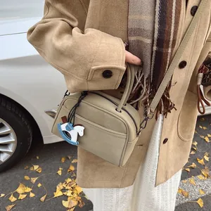 Retro beige leather crossbody bag with wooden horse charm in an autumn outdoor setting