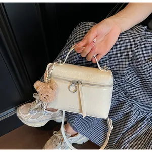 Detail view of cream handbag with pleated texture, silver hardware and plush bear charm