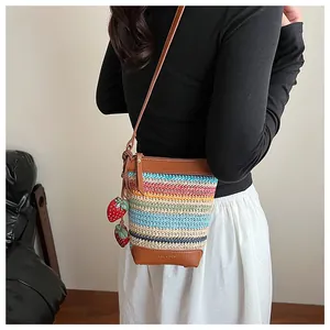 Close-up of colorful striped woven bag with brown leather trim and strawberry charms